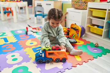 Wall Mural - Adorable hispanic toddler playing with car toy sitting on floor at kindergarten