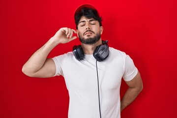 Wall Mural - Hispanic man with beard wearing gamer hat and headphones stretching back, tired and relaxed, sleepy and yawning for early morning