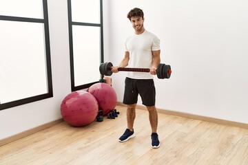 Sticker - Young hispanic man smiling confident training with dumbbell at sport center