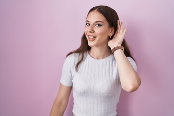 Sticker - Young hispanic girl standing over pink background smiling with hand over ear listening an hearing to rumor or gossip. deafness concept.