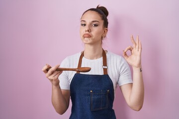 Wall Mural - Young hispanic girl wearing professional cook apron holding wood spoon depressed and worry for distress, crying angry and afraid. sad expression.