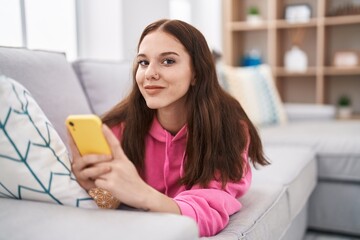 Sticker - Young woman using smartphone lying on sofa at home