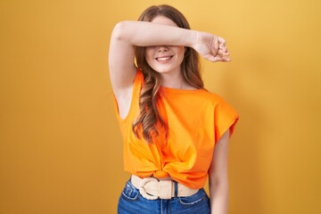 Poster - Caucasian woman standing over yellow background covering eyes with arm smiling cheerful and funny. blind concept.