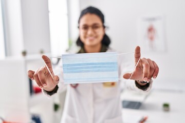 Sticker - Young latin woman wearing doctor uniform holding medical mask at clinic