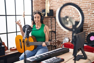 Sticker - Young hispanic woman musician recording classical guitar lesson by the smartphone at music studio