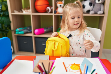 Sticker - Adorable blonde girl preschool student smiling confident opening backpack at kindergarten