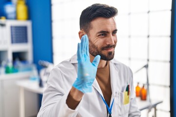 Sticker - Young hispanic man wearing scientist uniform saying hello with hand at laboratory