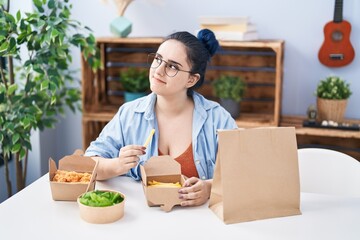 Poster - Young caucasian woman eating take away food sitting on table at home