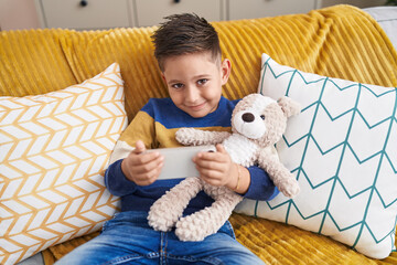 Canvas Print - Adorable hispanic boy hugging teddy bear watching video on smartphone at home