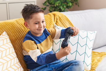 Canvas Print - Adorable hispanic boy playing video game sitting on sofa at home