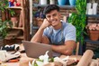 © Krakenimages.com - Young hispanic man florist smiling confident using laptop at flower shop
