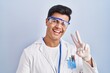 © Krakenimages.com - Hispanic man working as scientist smiling looking to the camera showing fingers doing victory sign. number two.