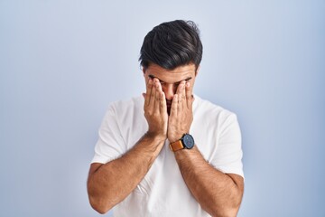 Poster - Hispanic man standing over blue background rubbing eyes for fatigue and headache, sleepy and tired expression. vision problem