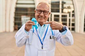 Canvas Print - Senior doctor with grey hair holding blue ribbon smiling happy pointing with hand and finger