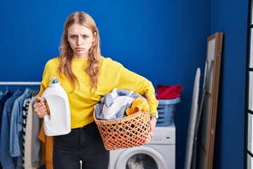 Poster - Young caucasian woman holding laundry basket and detergent bottle depressed and worry for distress, crying angry and afraid. sad expression.