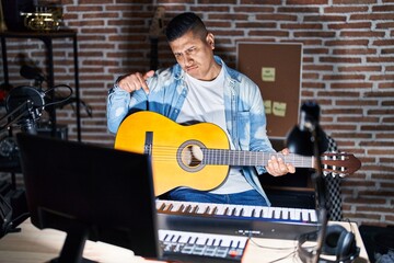 Wall Mural - Hispanic young man playing classic guitar at music studio pointing down looking sad and upset, indicating direction with fingers, unhappy and depressed.