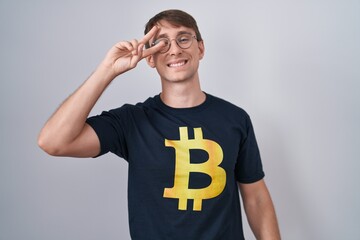 Sticker - Caucasian blond man wearing bitcoin t shirt doing peace symbol with fingers over face, smiling cheerful showing victory