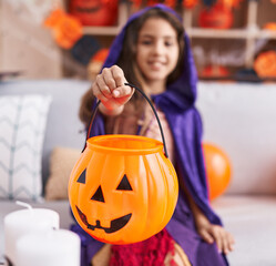 Sticker - Adorable hispanic girl wearing halloween costume holding pumpkin basket at home