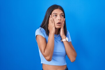 Wall Mural - Brunette young woman standing over blue background tired hands covering face, depression and sadness, upset and irritated for problem