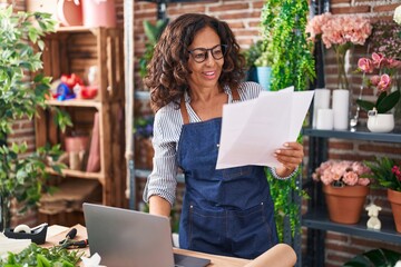 Wall Mural - Middle age woman florist using laptop reading document at flower shop