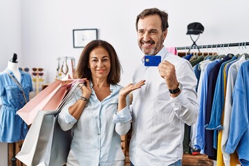 Poster - Hispanic middle age couple holding shopping bags and credit card smiling cheerful presenting and pointing with palm of hand looking at the camera.