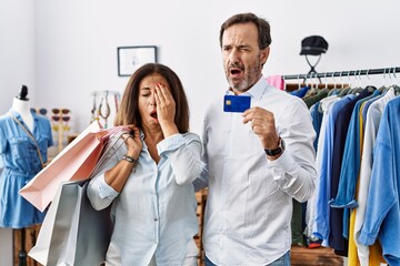 Canvas Print - Hispanic middle age couple holding shopping bags and credit card yawning tired covering half face, eye and mouth with hand. face hurts in pain.