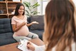 © Krakenimages.com - Young pregnant woman at therapy session amazed and smiling to the camera while presenting with hand and pointing with finger.