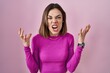 Hispanic woman standing over pink background crazy and mad shouting and yelling with aggressive expression and arms raised. frustration concept.