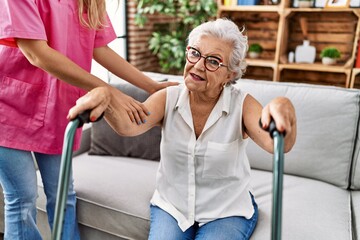 Senior grey-haired woman patient supported for nurse and walker at geriatric