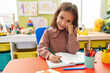 © Krakenimages.com - Adorable hispanic girl preschool student sitting on table writing on notebook at kindergarten