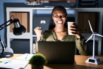 Poster - African woman working using computer laptop at night very happy and excited doing winner gesture with arms raised, smiling and screaming for success. celebration concept.