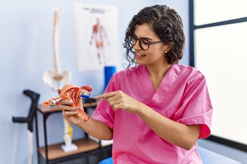 Poster - Young latin woman wearing physiotherapist uniform holding anatomical model of uterus at clinic