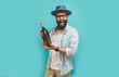 © San4ezz007 - Young bearded charismatic hipster somilier showing a big bottle of wine, isolated on a blue studio background. Wine presentation.