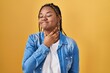 African american woman with braids standing over yellow background touching painful neck, sore throat for flu, clod and infection