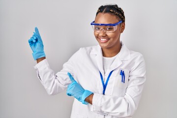 Poster - African american woman with braids wearing scientist robe smiling and looking at the camera pointing with two hands and fingers to the side.