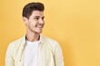 © Krakenimages.com - Young hispanic man standing over yellow background looking away to side with smile on face, natural expression. laughing confident.