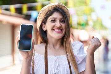 Wall Mural - Young brunette woman holding smartphone showing blank screen screaming proud, celebrating victory and success very excited with raised arm