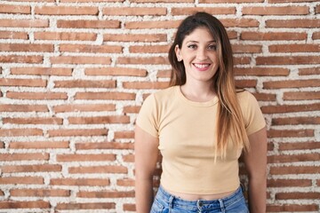 Poster - Young brunette woman standing over bricks wall with a happy and cool smile on face. lucky person.