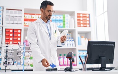 Canvas Print - Young hispanic man pharmacist holding pills using credit card and dataphone at pharmacy