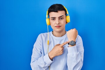 Poster - Non binary person listening to music using headphones in hurry pointing to watch time, impatience, looking at the camera with relaxed expression