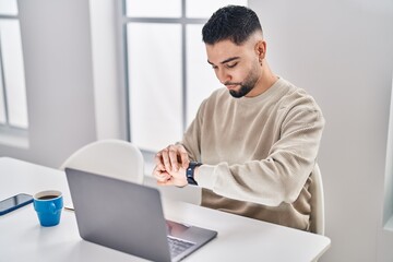 Sticker - Young arab man looking watch sitting on table working at home