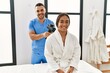 © Krakenimages.com - Latin man and woman wearing physiotherapy uniform massaging neck using percussion gun at beauty center