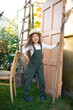© Анна Брусницына - a vertical portrait of a cute funny blue-eyed farmer girl in a hat with long hair and a green jumpsuit. Horticulture. Hobby. Lifestyle.