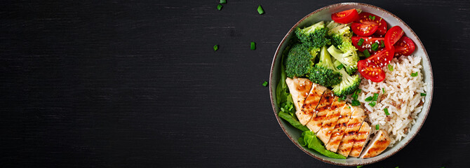 Delicious buddha bowl with grilled chicken, fresh vegetables and rice on a dark background. Top view, banner