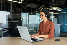 Smiling Hispanic Businesswoman Working Inside Office With Laptop And Headset For Video Call, Woman Sitting At Workplace Happy Working With Clients.