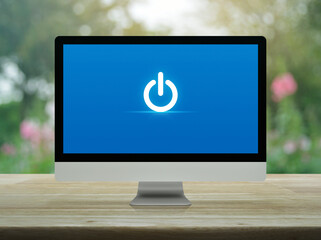 Wall Mural - Power button icon on desktop modern computer monitor screen on wooden table over blur pink flower and tree in park, Business start up online concept