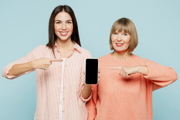 Wall Mural - Elder smiling parent mom with young adult daughter two women together wear casual clothes show hold use mobile cell phone with blank screen area isolated on plain blue background. Family day concept.