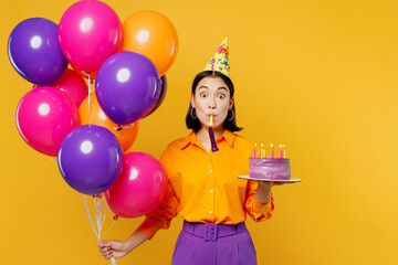 Wall Mural - Happy fun amazed young woman in casual clothes hat celebrating hold bunch of colorful air balloons cake with candles blow pipe isolated on plain yellow background Birthday 8 14 holiday party concept