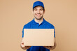 © ViDi Studio - Professional smiling cheerful fun delivery guy employee man wear blue cap t-shirt uniform workwear work as dealer courier hold cardboard box isolated on plain light beige background. Service concept
