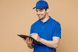 © ViDi Studio - Professional fun delivery guy employee man wear blue cap t-shirt uniform workwear work as dealer courier hold clipboard with papers document isolated on plain light beige background. Service concept.